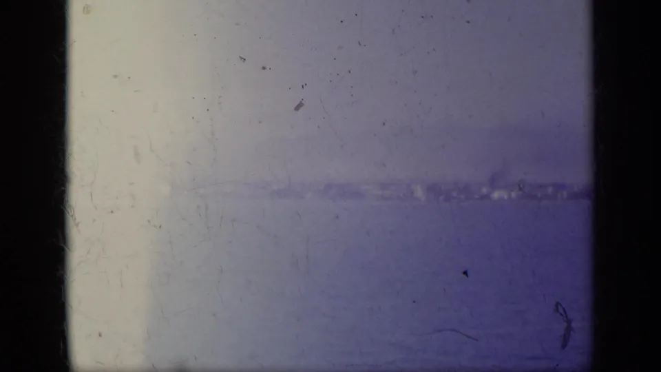 1963 Greece waterfront view with a pale distant shoreline, open water and visible 8mm frame edges.