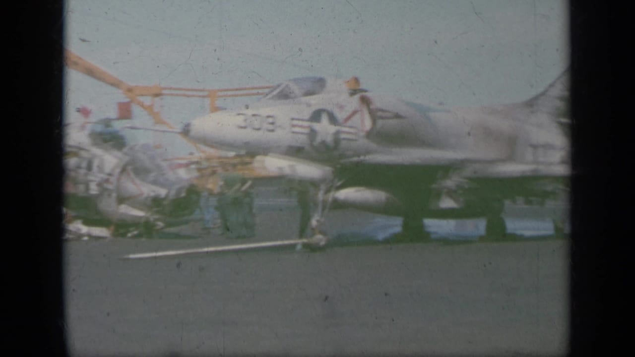 Jet marked 309 beside a yellow crane on an aircraft carrier deck.