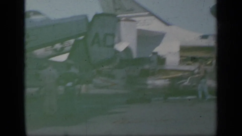 1963 Greece 8mm view of parked military-style aircraft on pavement, partly obscured by green color shift, dust, and film-frame edges.
