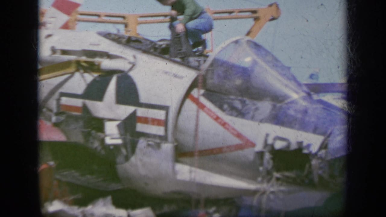 1963 Greece 8mm frame showing a white U.S. military jet fighter on deck with star insignia, open panels, and a crew member near the cockpit.