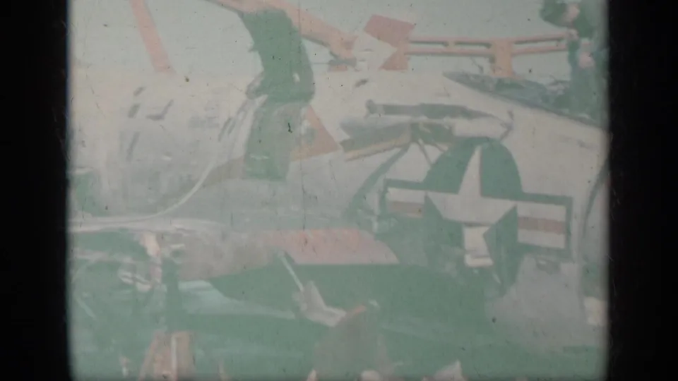 Faded 8mm frame from the 1963 Greece clip showing a white U.S. military jet with star insignia and nearby carrier deck equipment.