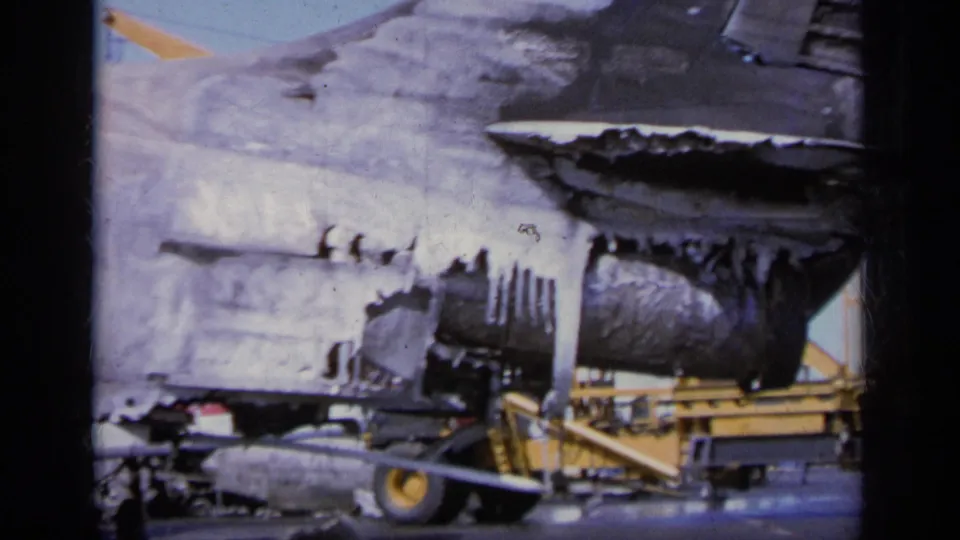1963 Greece 8mm frame showing the burned rear area of a military jet, nearby deck gear, and visible film scratches.