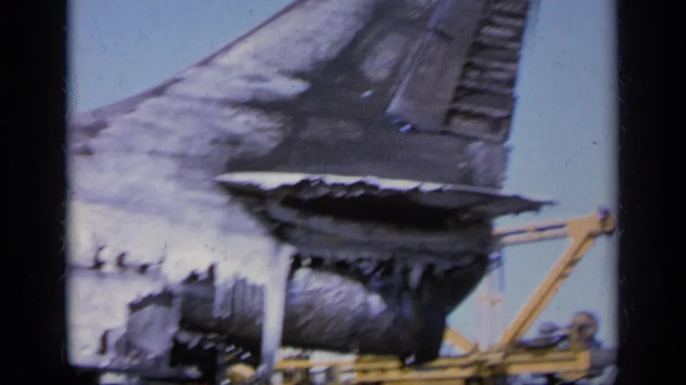 Greece 1963 8mm frame showing severe burn damage on an aircraft rear section with yellow support equipment nearby.
