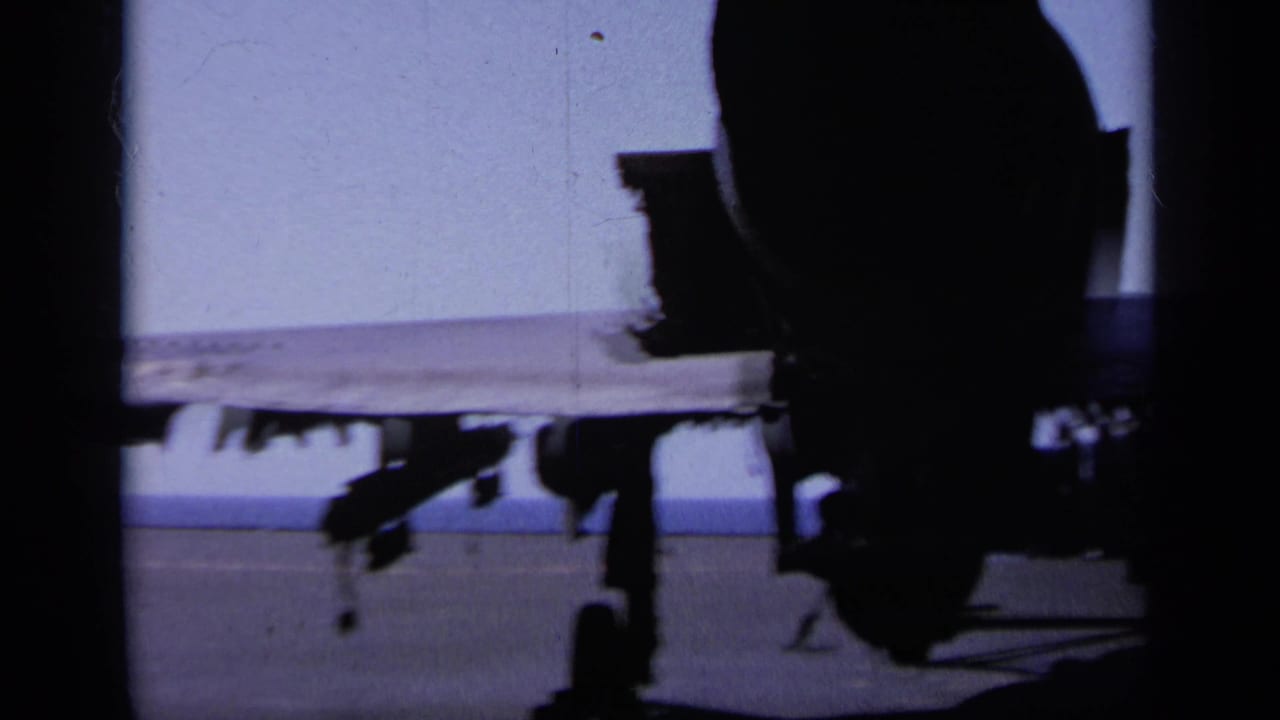 Aircraft landing gear and underside silhouetted on a carrier deck.