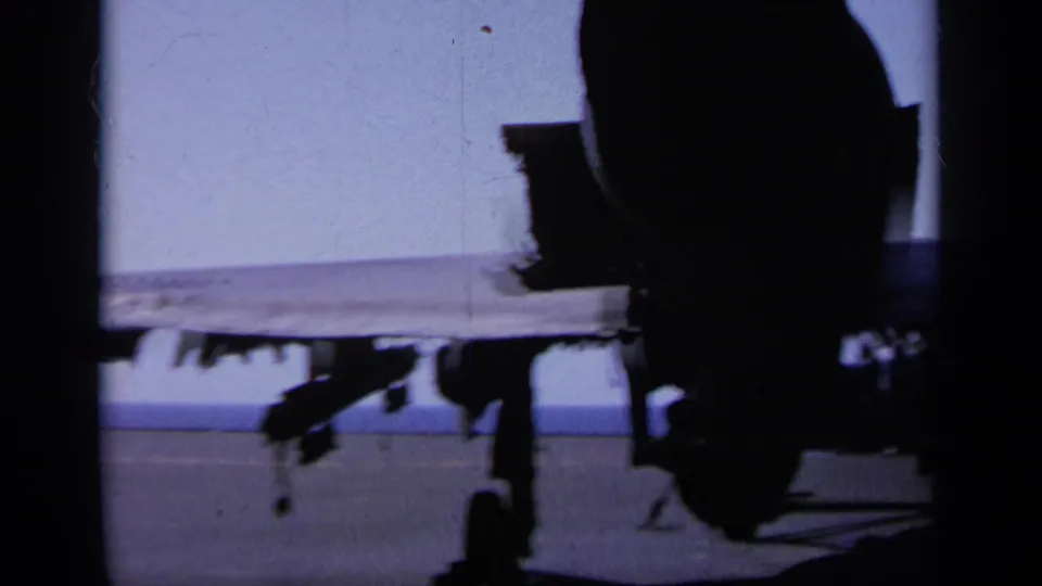 Greece 1963 frame showing the underside and landing gear of a military aircraft on a carrier deck in harsh daylight.