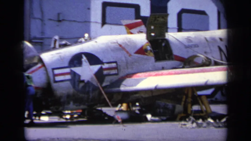 Closer 1963 Greece frame of a marked U.S. Navy jet on deck, with crew partly visible near the fuselage and equipment below.