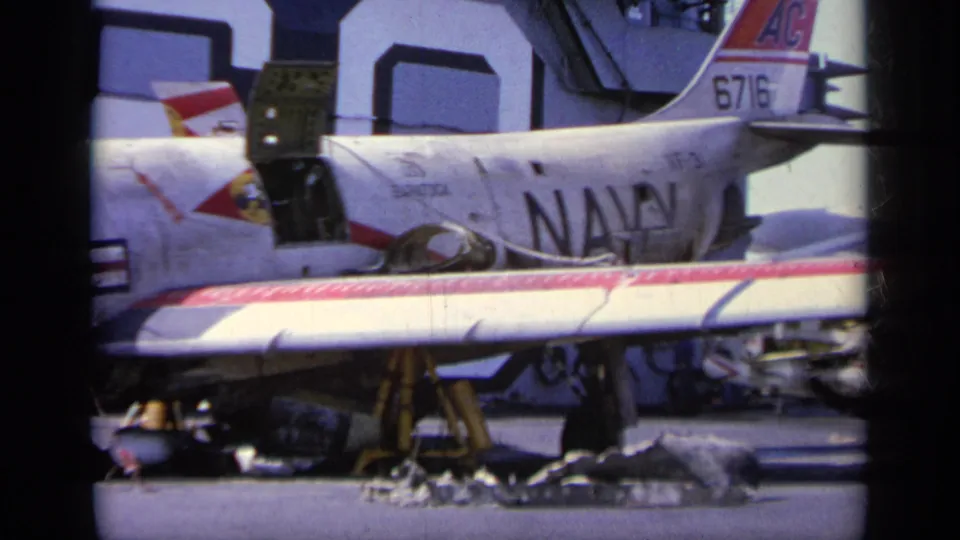 Side view of a U.S. Navy jet in 1963 Greece footage, with tail number 6716, open access area, and equipment on the carrier deck.