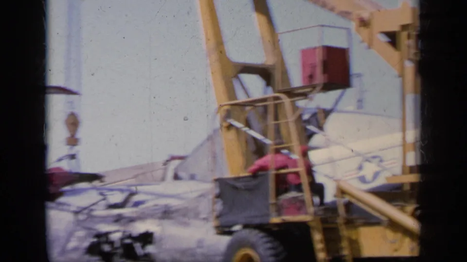 1963 Greece 8mm frame showing yellow recovery equipment near the damaged Navy aircraft as cleanup continues on the airfield surface.