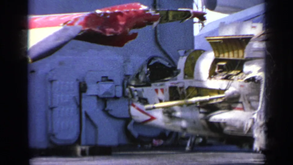 1963 Greece 8mm frame showing a red damaged aircraft section near wreckage and ship equipment during deck salvage.