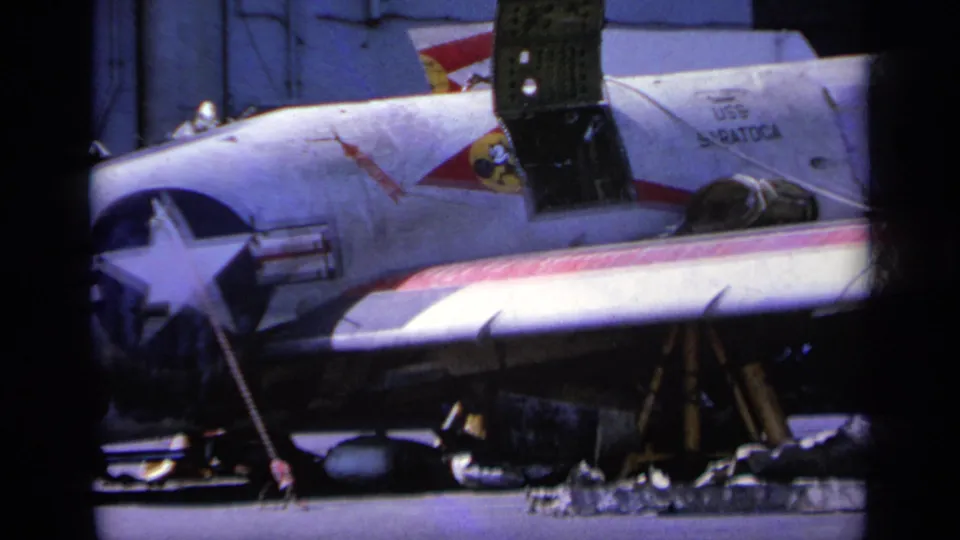 1963 Greece 8mm frame showing a U.S.-marked military aircraft on an airfield with support equipment nearby.