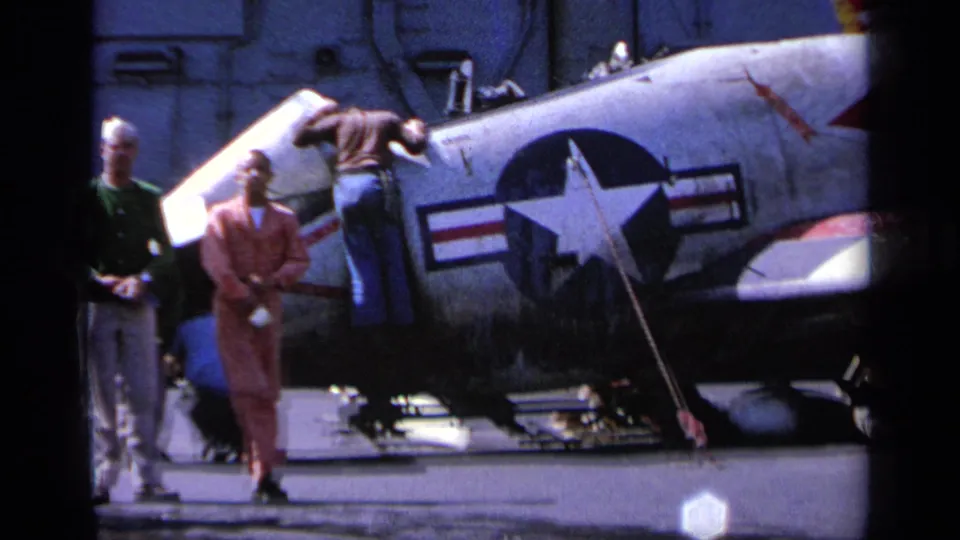 1963 Greece 8mm frame with men near a U.S.-marked military aircraft, including one person climbing or working on the wing.