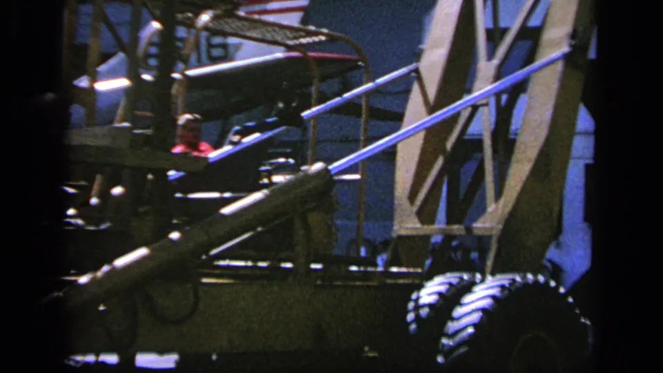 1963 Greece 8mm frame showing ground equipment, stairs, wheels, and partial aircraft structures at an airfield.