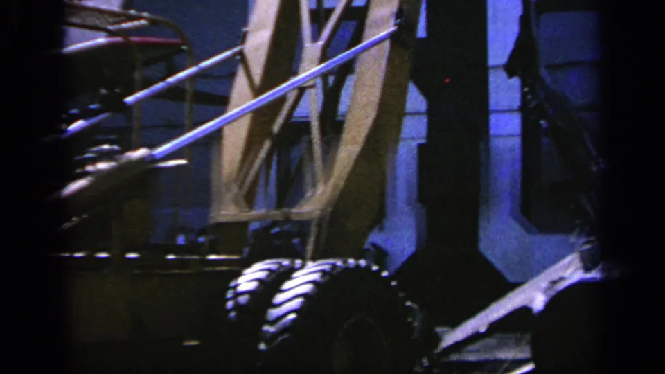 1963 Greece 8mm frame focused on airfield support equipment and partial aircraft structures, with dark edge framing.