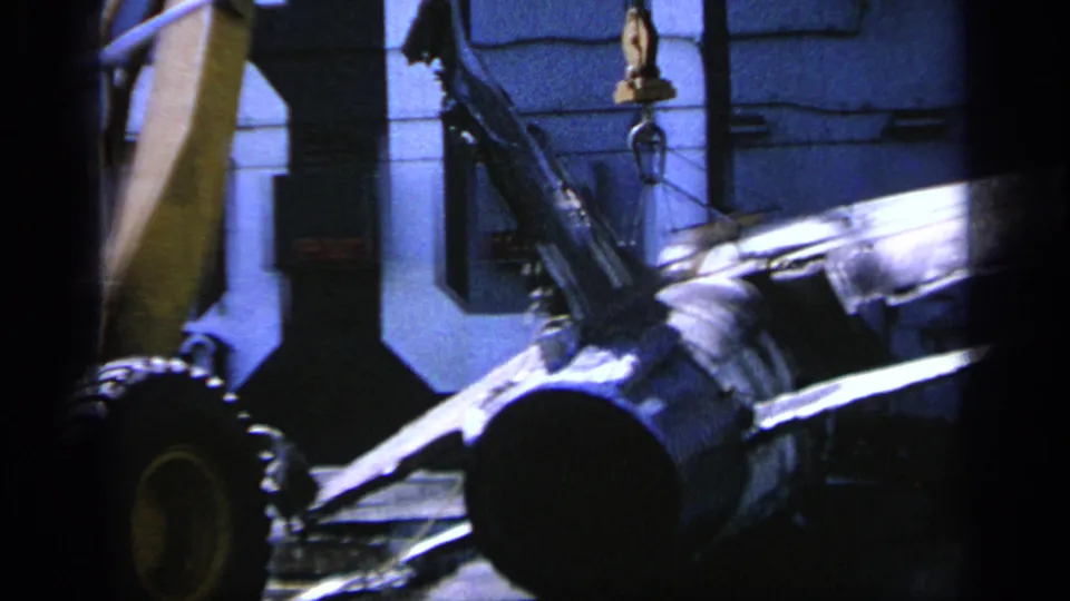 1963 Greece industrial footage frame with a heavy cylindrical component appearing to be lifted or positioned by crane rigging.