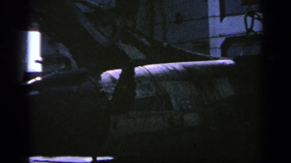 1963 Greece 8mm frame showing part of a camouflaged military helicopter in a dim indoor hangar-like space.