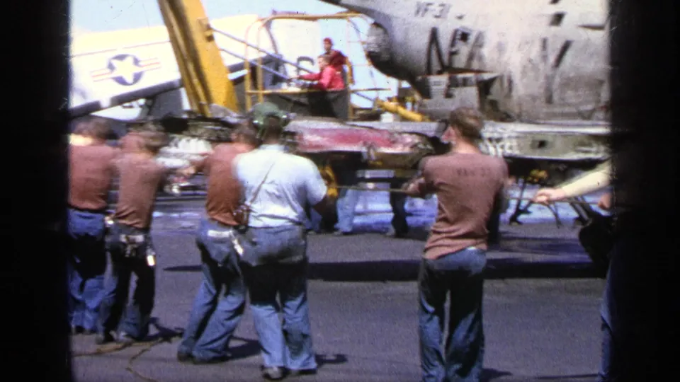 1963 Greece airfield view with men in jeans and shirts near military aircraft parts and a visible star-marked tail section.