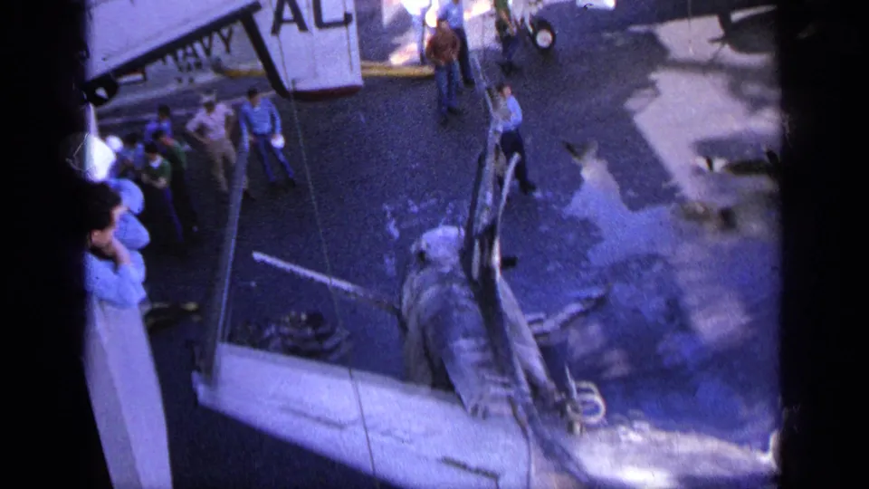 1963 Greece frame showing crew gathered around a damaged aircraft and torn wing on a carrier deck.