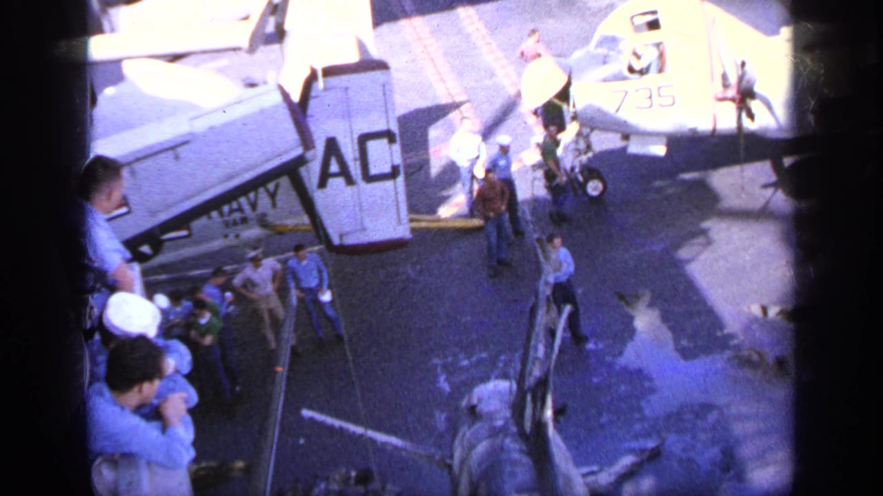 1963 Greece 8mm frame showing personnel gathered near U.S. marked aircraft on an airfield tarmac.