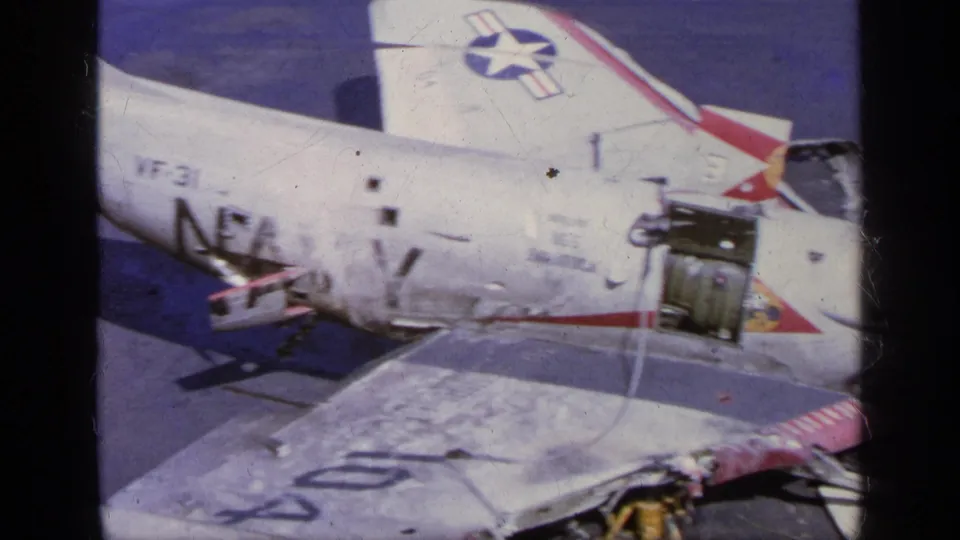 1963 Greece 8mm frame showing the Starfighter side, wing surface, open service panels, and damaged aircraft area on the tarmac.
