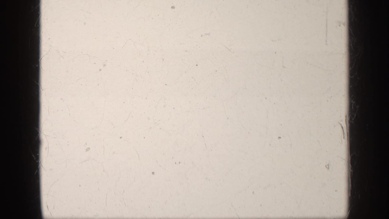 Overexposed 8mm film frame from the clip start, showing dark gate edges, scratches, dust, and no distinct subject.