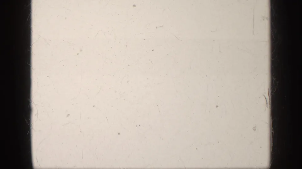 Overexposed 8mm film frame from the clip start, showing dark gate edges, scratches, dust, and no distinct subject.
