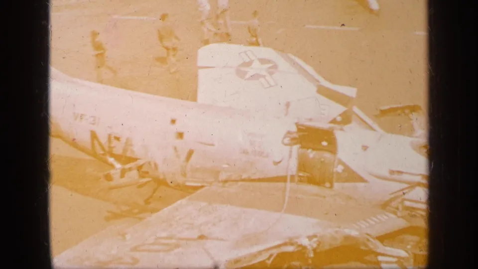 1963 Greece reel frame showing a U.S. military aircraft on a deck or airfield, partly overexposed with insignia and scattered parts visible.