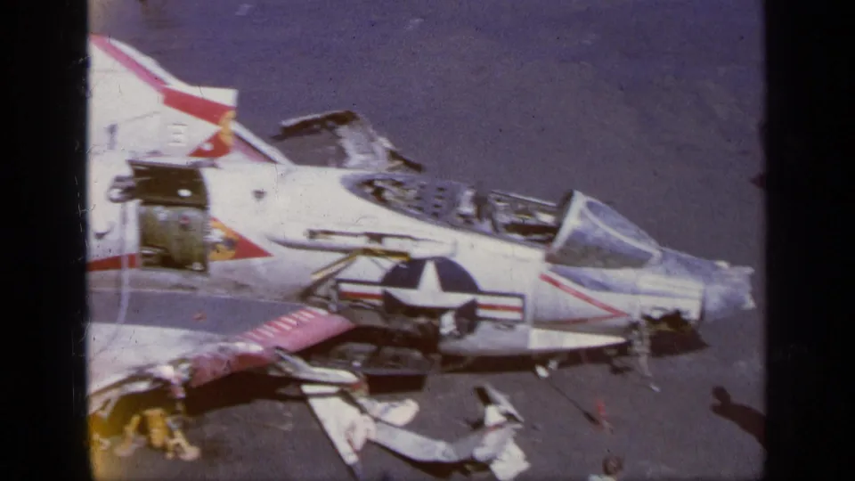 1963 Greece reel frame showing a U.S. Navy-style aircraft with visible insignia, cockpit area, and debris or removed panels nearby.
