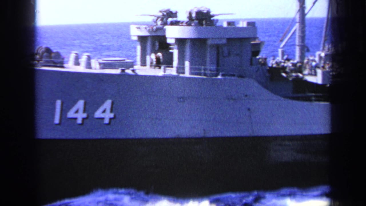Side of a gray naval ship marked 144 with deck structures and sea beyond.