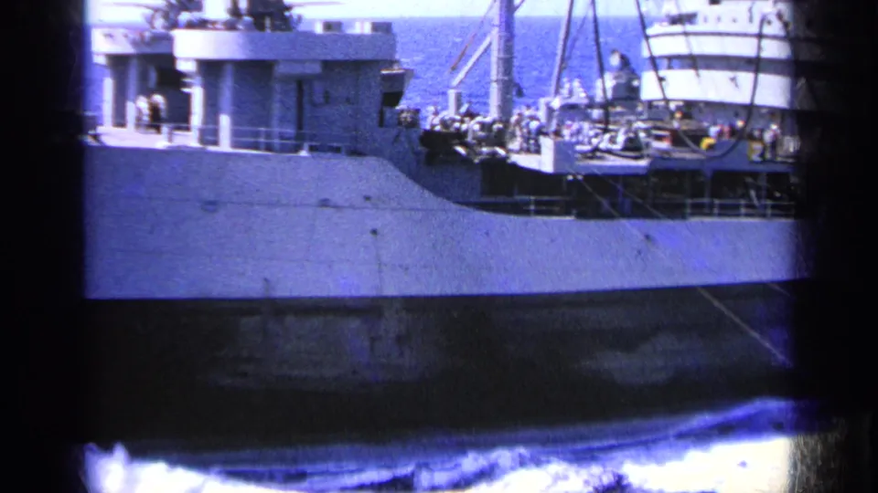 1963 Greece 8mm view of the naval ship's deck area, with crew members, rigging, and ship equipment visible along the hull.