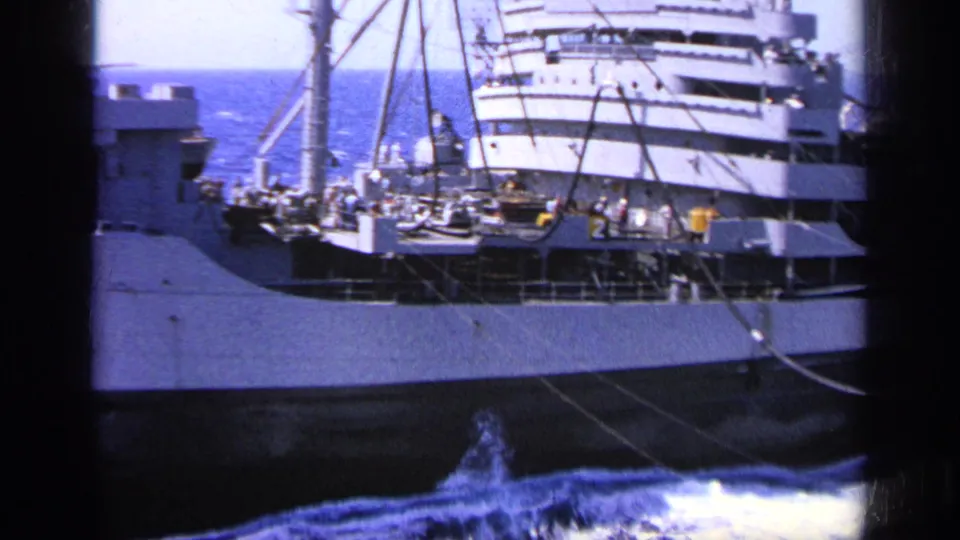 Close 8mm frame of a naval ship deck in Greece, with crew gathered near rigging, a small boat, and upper ship structure.
