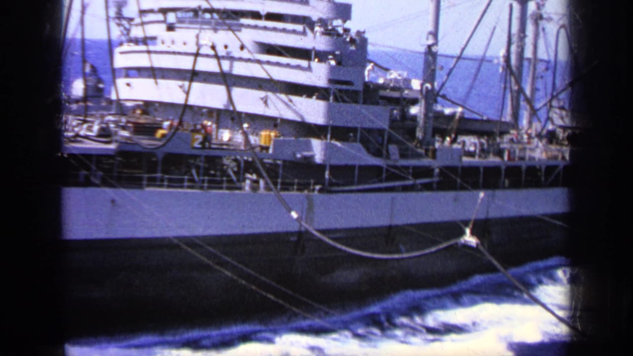 Cargo ship broadside with deck rigging, small crew figures, blue sea, and dark film borders.