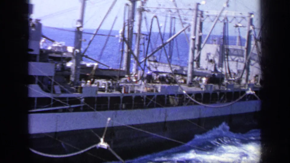 1963 Greece 8mm frame of the cargo ship's side deck and rigging, with small crew figures above rough blue water.