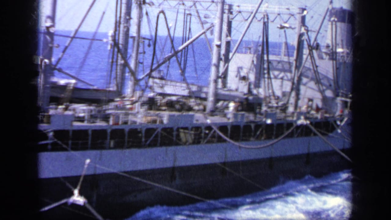 1963 Greece 8mm frame showing a cargo ship moving beside the camera vessel, with rigging, cables, hull, and foaming sea visible.