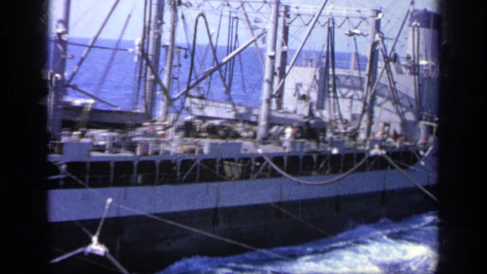 1963 Greece 8mm frame showing a cargo ship moving beside the camera vessel, with rigging, cables, hull, and foaming sea visible.