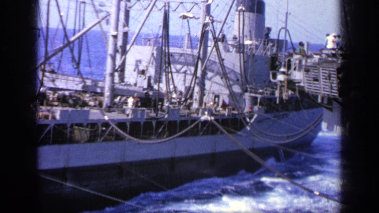 Cargo ship deck and stern area with rigging, railings, and foaming sea.