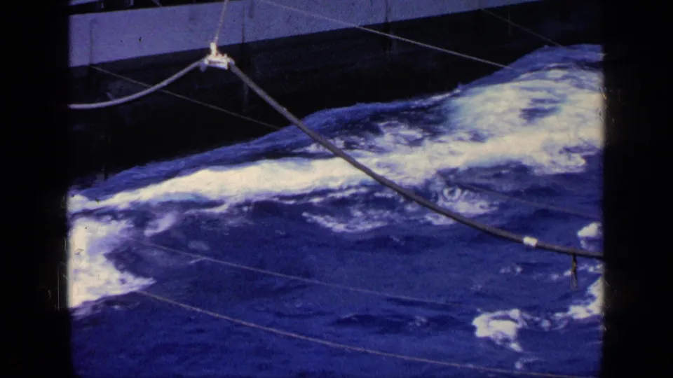 1963 Greece 8mm frame of turbulent water beside a vessel, seen through dark framing with suspended cables and ship hardware visible.