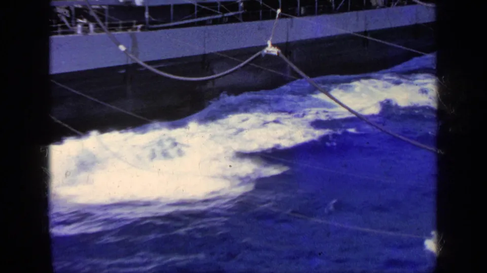 1963 Greece 8mm frame showing a close deck-side view of white sea foam, dark blue water, and crossing rigging lines on a moving boat.