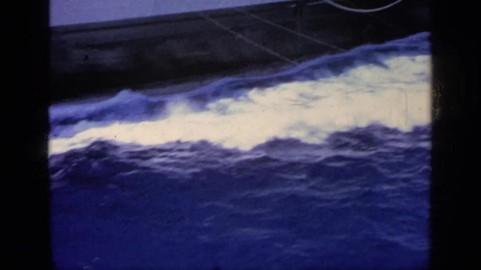 1963 Greece 8mm frame with blue ocean swell and white foam along the boat, partially obscured by a dark vertical foreground strip.