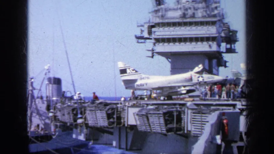 1963 Greece 8mm frame showing a naval deck with parked aircraft, visible personnel, and the ship island structure.