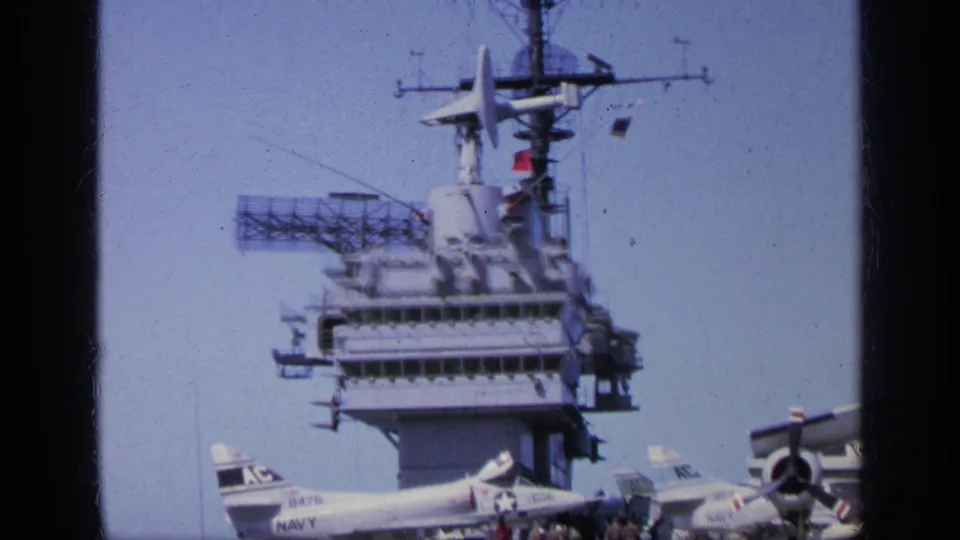 1963 Greece 8mm frame showing a carrier-like island, radar equipment, aircraft tails, and small personnel on deck.