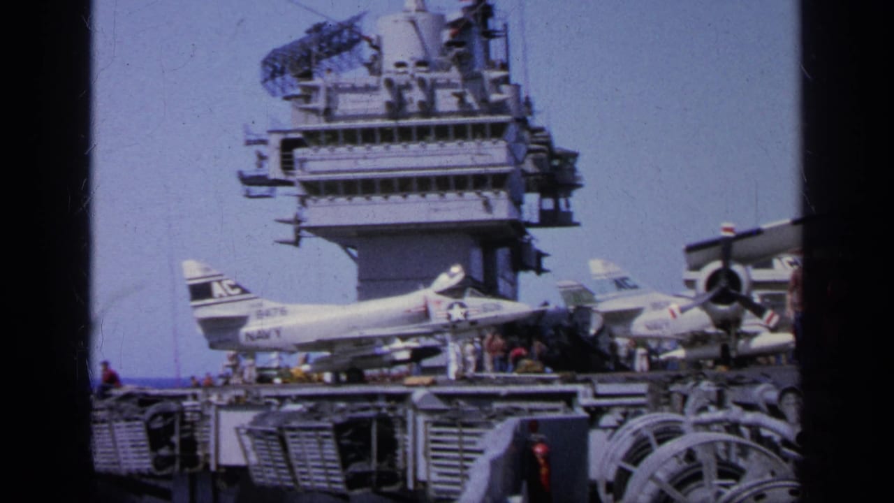 1963 Greece 8mm frame showing a U.S. Navy aircraft carrier deck with parked jet aircraft, crew figures, and radar structures above.