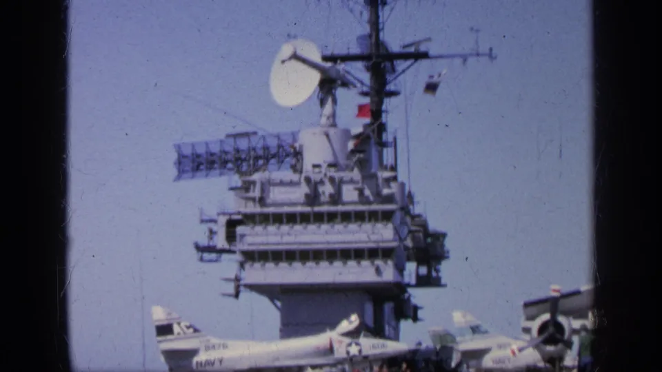 Home-movie frame from the 1963 Greece clip showing a carrier island, radar equipment, and part of a parked Navy jet below.