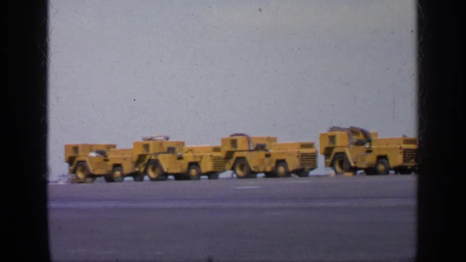 1963 Greece 8mm frame with several yellow aircraft tow vehicles lined across a carrier deck under an open sky.