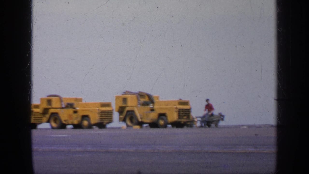 Yellow ground support vehicles sit on a wide tarmac near a distant crew member.