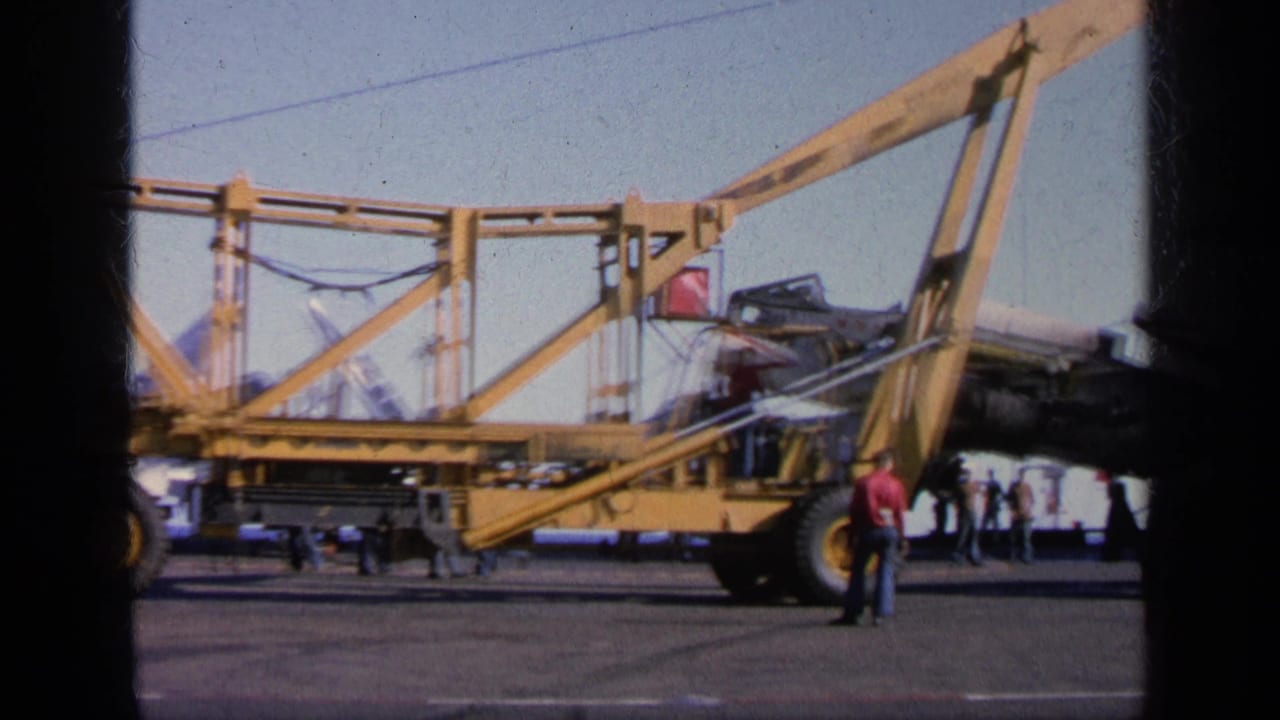 1963 Greece 8mm frame showing a yellow deck crane positioned near a damaged military aircraft while people stand on the carrier deck.