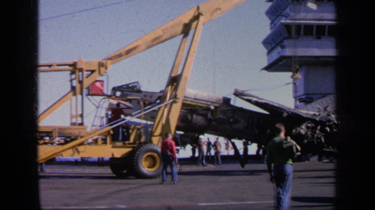 Damaged aircraft under a yellow crane near the carrier island structure.
