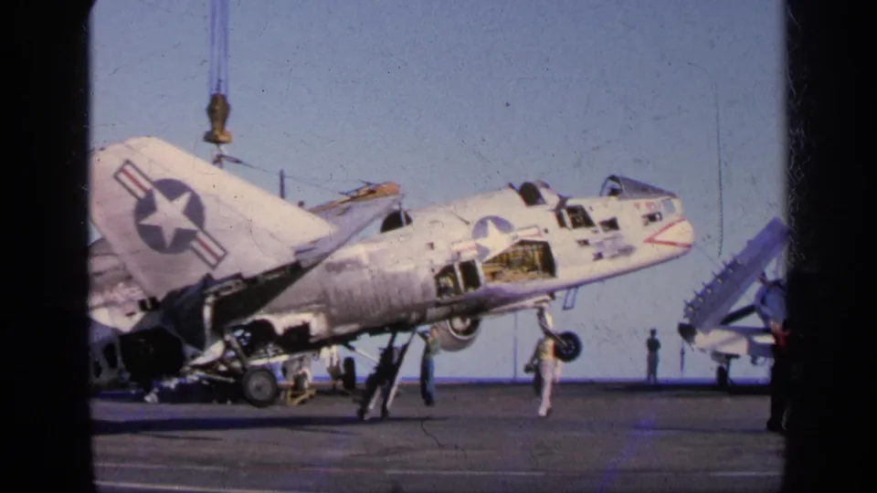 1963 Greece frame showing the damaged U.S.-marked aircraft from the side, with crew and another aircraft visible on the deck.
