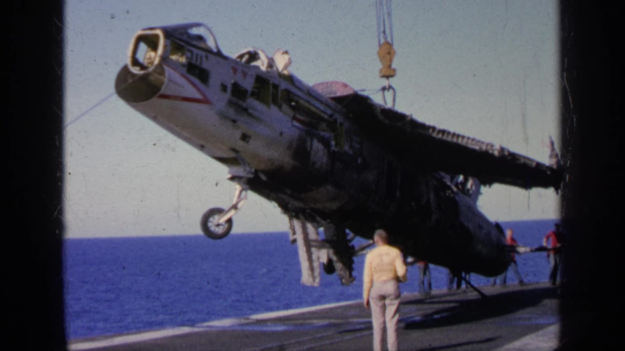 In Greece 1963 footage, a damaged aircraft hangs from a crane on a carrier deck while crew stand nearby at sea.