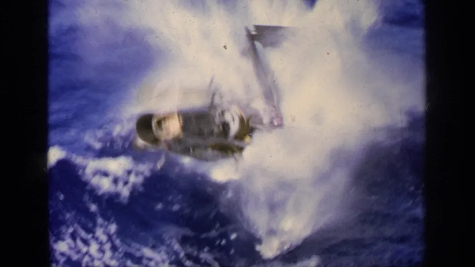 The damaged aircraft drops into the sea beside the carrier, throwing up a large splash in Greece 1963 footage.