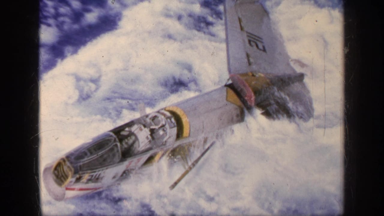 1963 Greece 8mm frame showing a marked military jet angled downward against bright clouds.